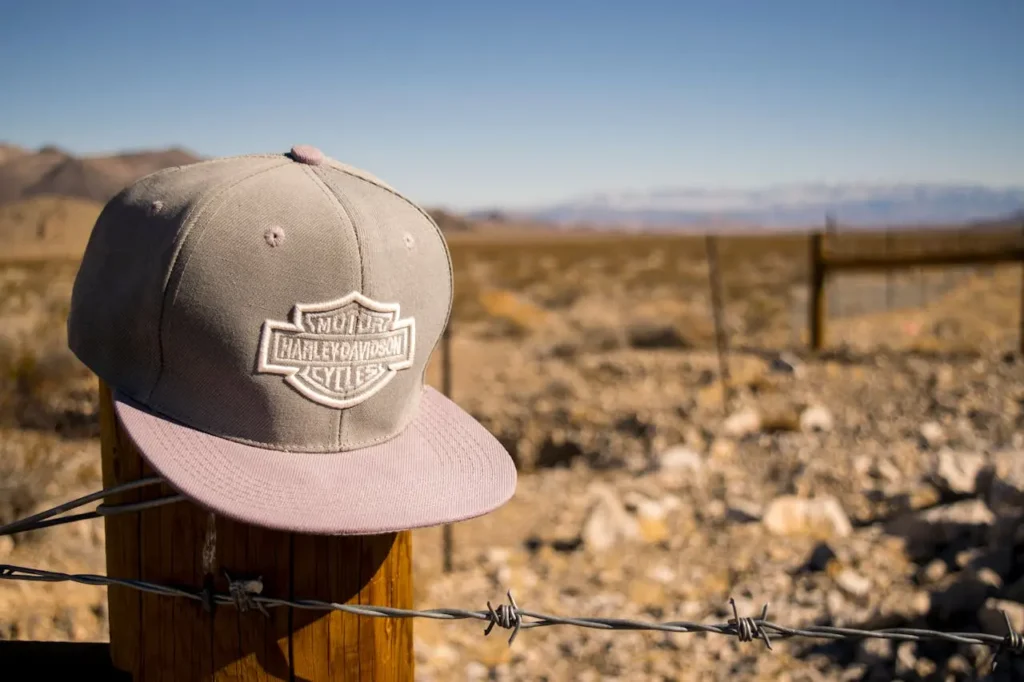 Flat Brim Cap of Gray Harley Davidson Motorcycles Hanging on Brown Wooden Fence with Gray Barbed Wire